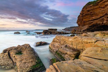 Rocky Beach at Dusk With Blurred Water, Golden Rocks, and Cloudy Sky — Lake Macquarie Mobile Locksmiths in Caves Beach, NSW