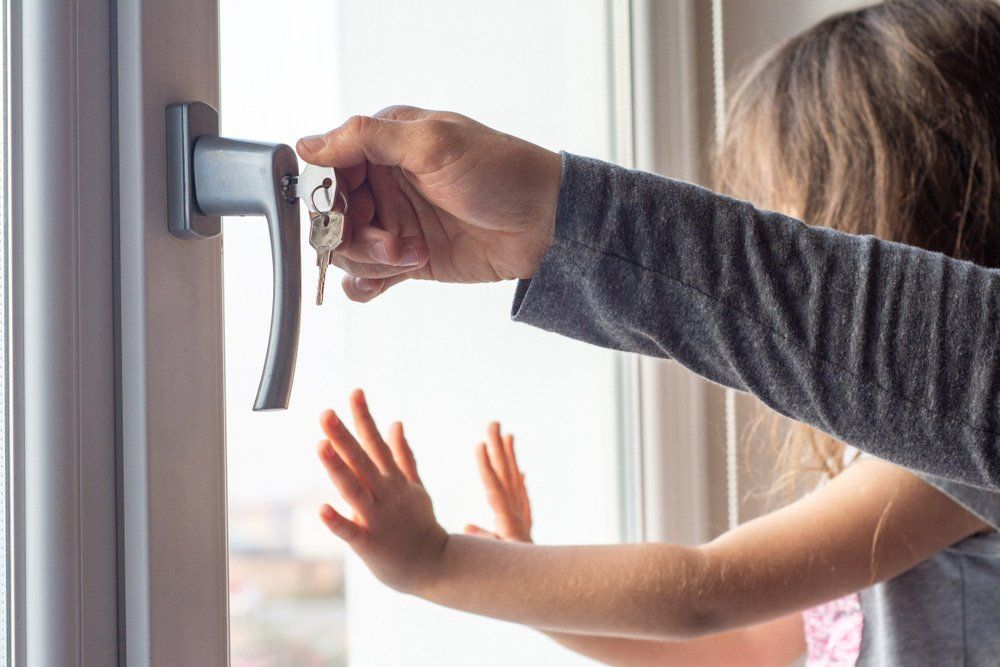 Person Unlocking a Window While a Child Reaches Toward It — Lake Macquarie Mobile Locksmiths in Cardiff, NSW