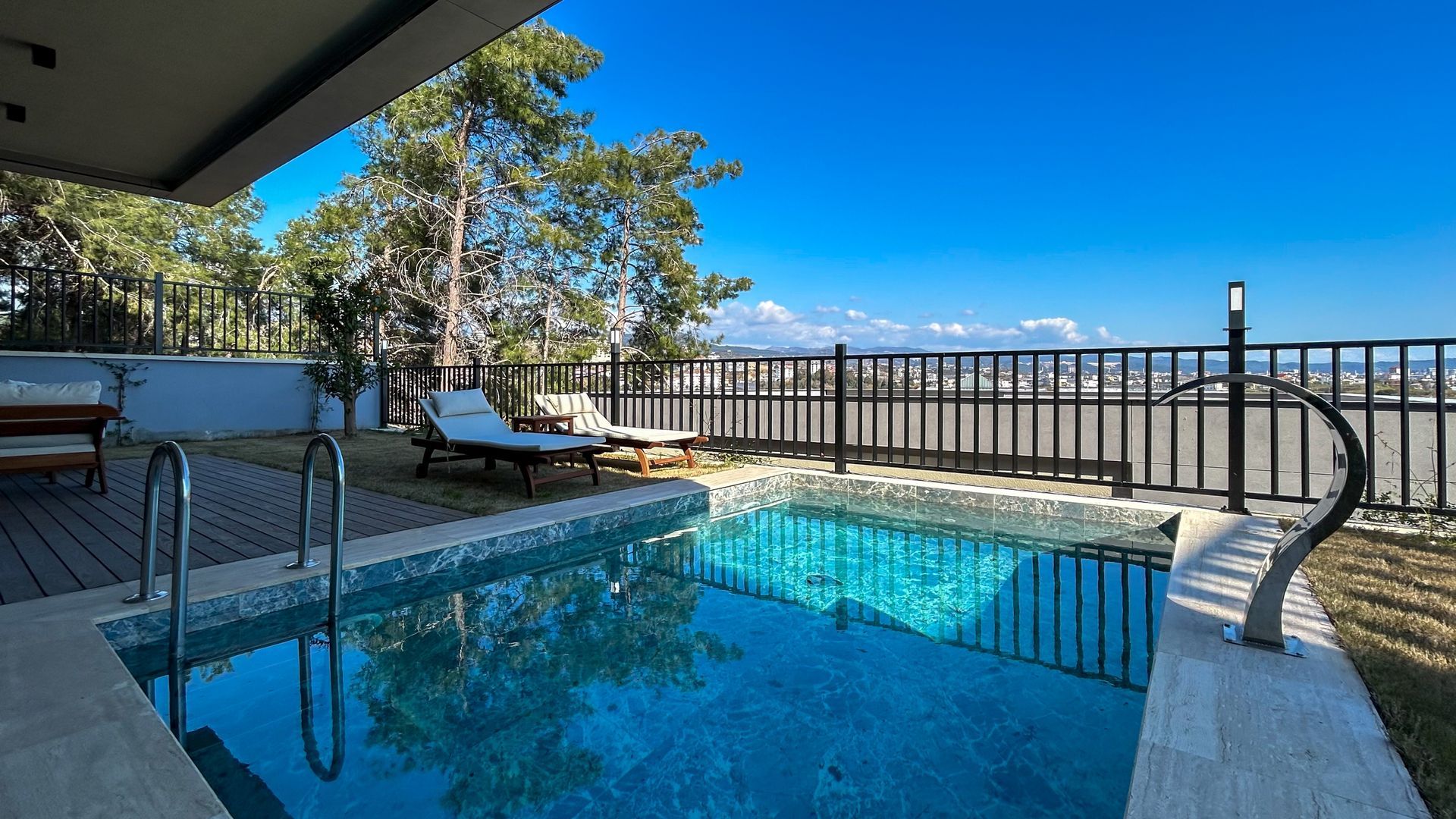 Small outdoor pool with lounge chairs and a view of a city on a bright, sunny day. — Gympie Fence Inspections in Rainbow Beach, QLD