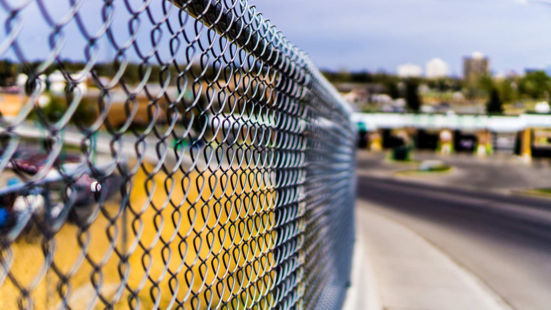 Close-up of a chain-link fence with a blurred roadside and vehicles in the background