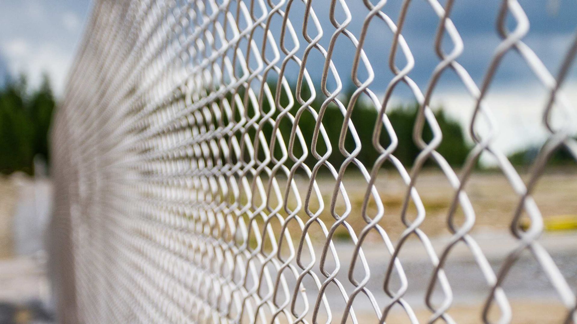 Close-up of a silver chain-link fence with a blurred outdoor street and buildings in the background