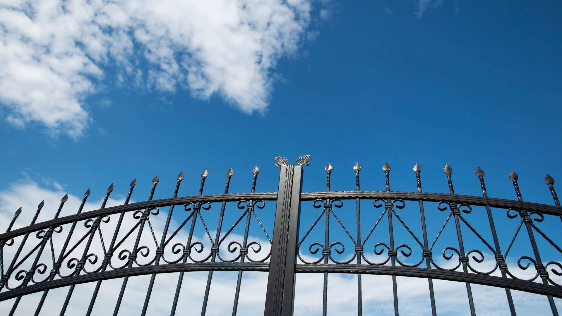 Black wrought-iron fence against a bright blue sky with scattered white clouds