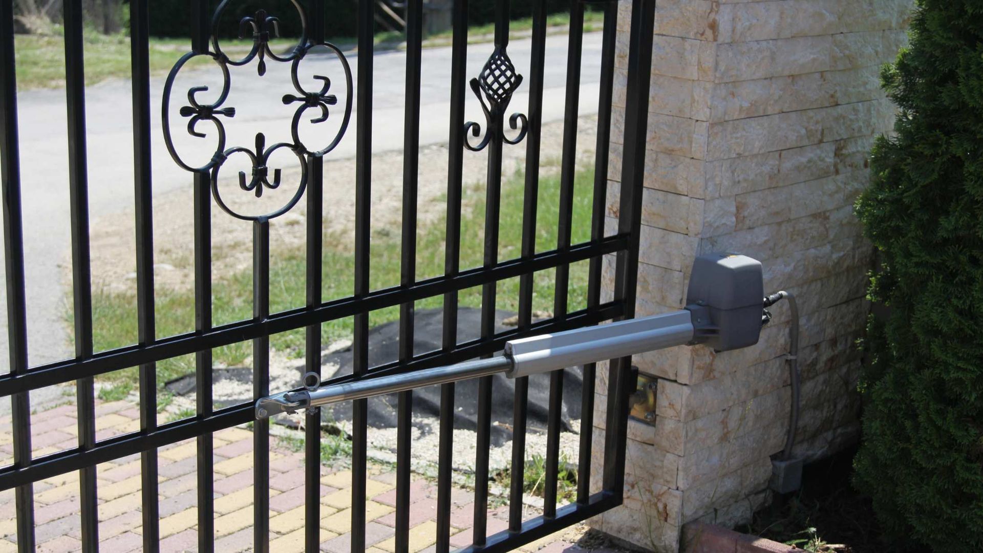 Automated gate opener mounted on a black iron driveway gate beside a brick pillar