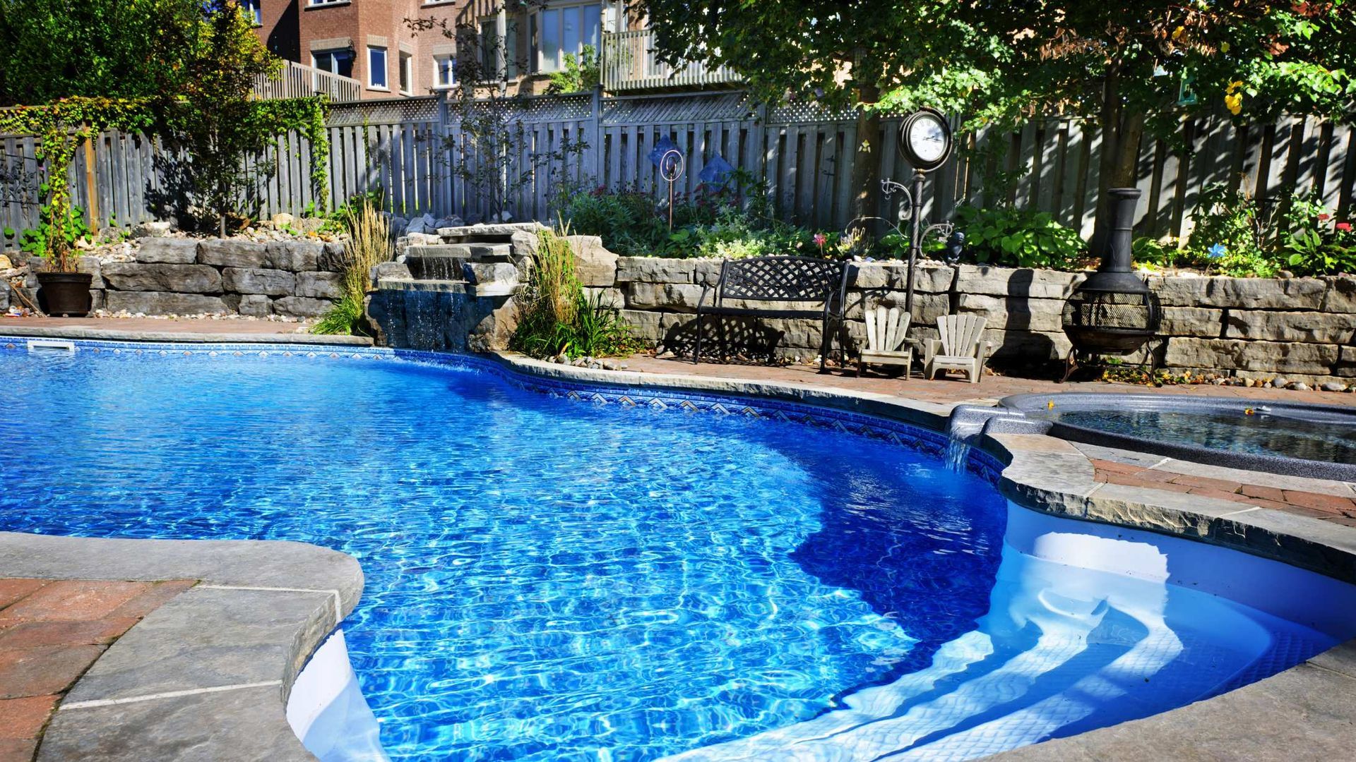 Backyard pool with blue water, stone deck, and patio seating under trees