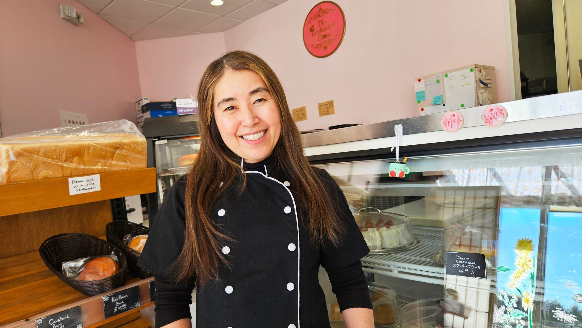 Smiling woman in black chef coat stands in bakery.