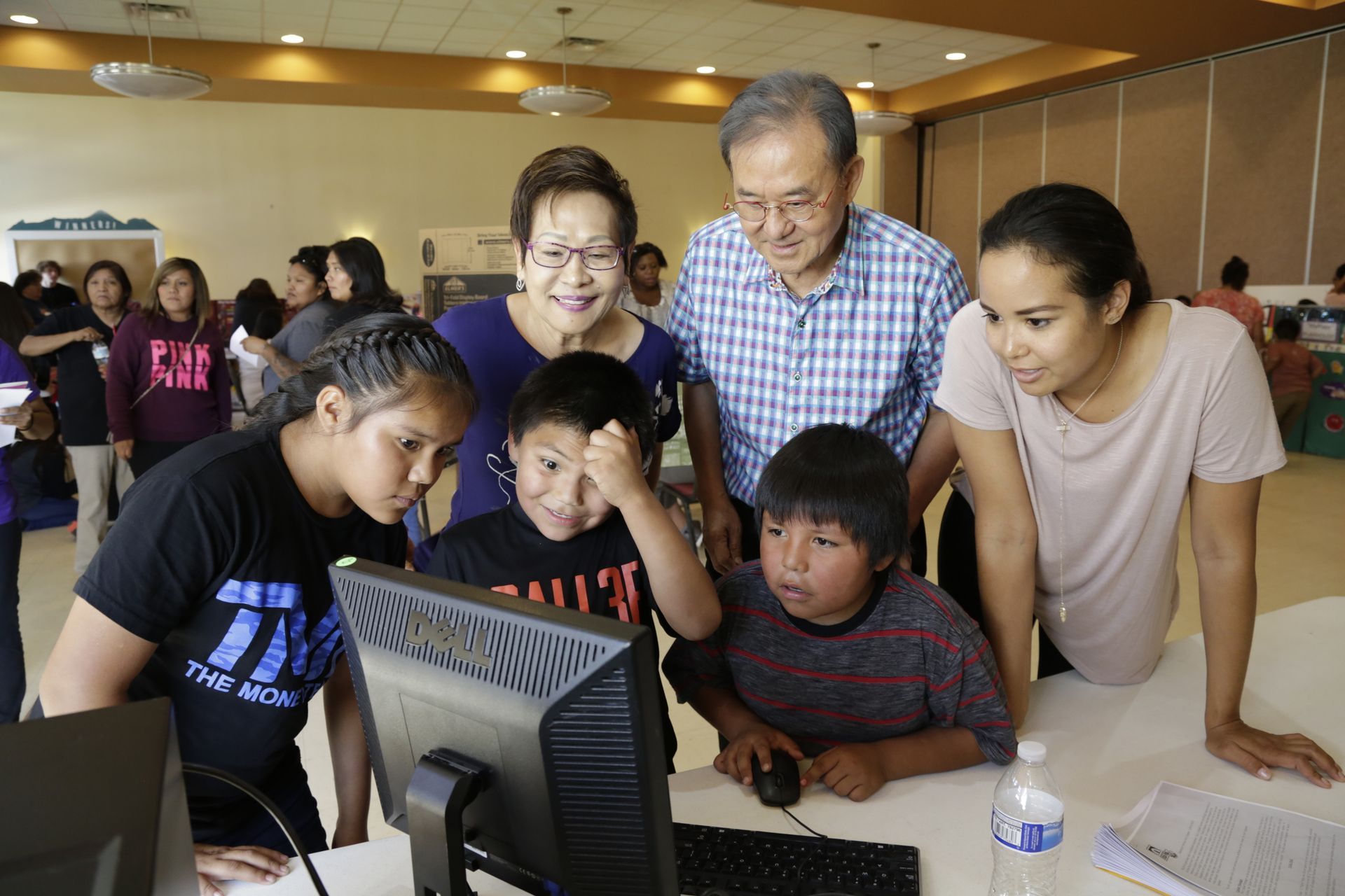 Family of six looking at a computer screen in a brightly lit room.
