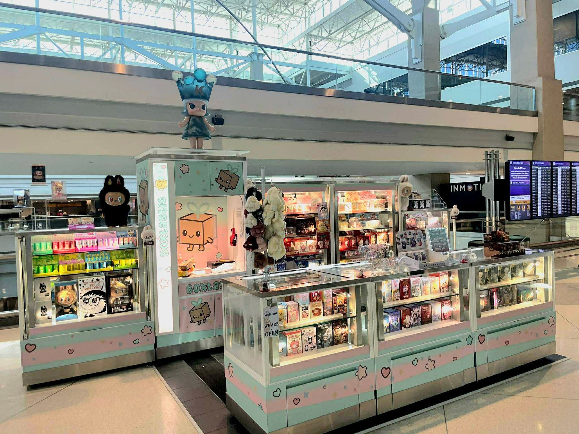 A Pop Mart kiosk in a mall featuring colorful shelves of collectible toy figures and a central claw machine game.
