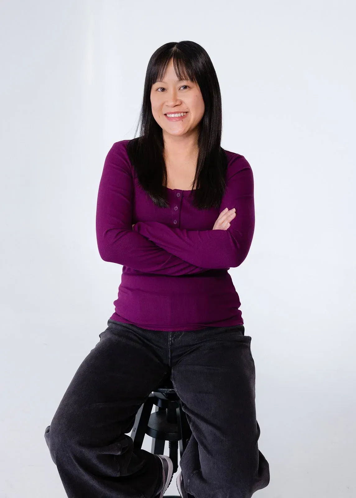 Joanne Liu, sits with arms crossed, smiling. White background.