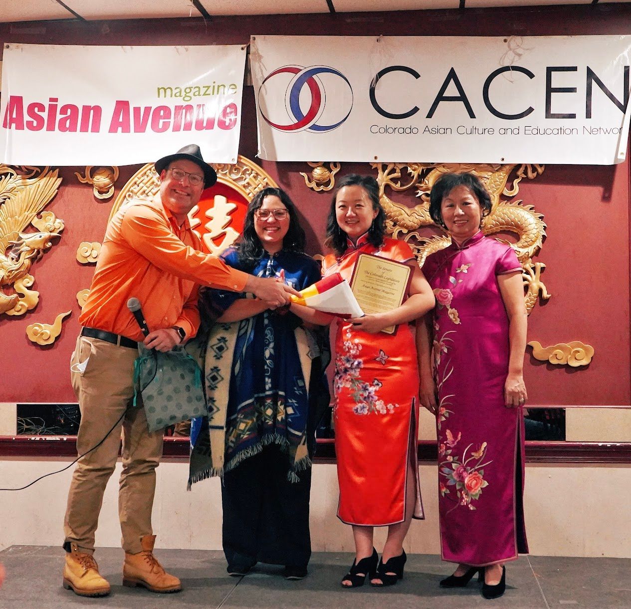 Four people pose in front of Asian Avenue and CACEN banners, holding a certificate and a red gift bag.