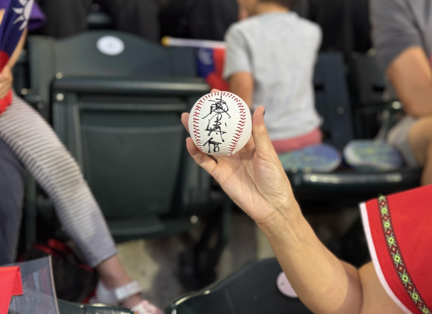 Person holding baseball with Chinese writing at a stadium.