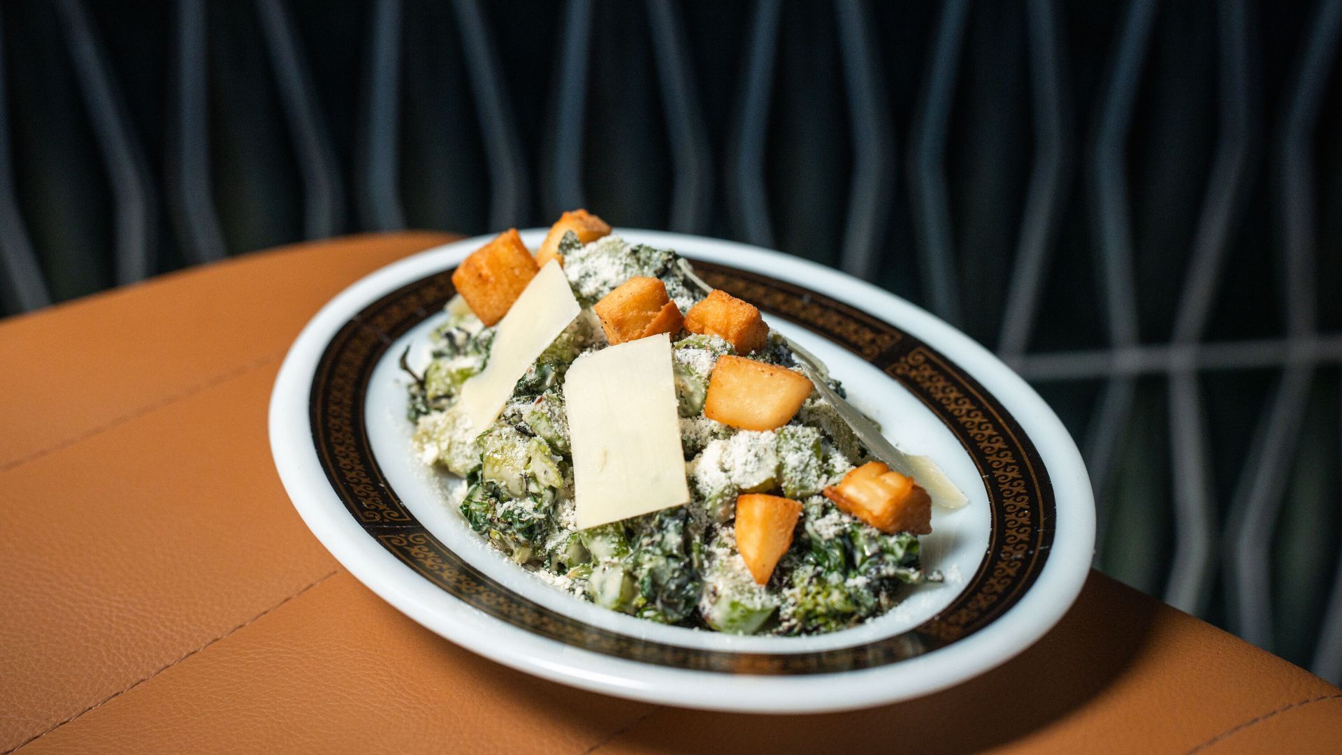 Salad with croutons and cheese in a brown-rimmed dish on a table.
