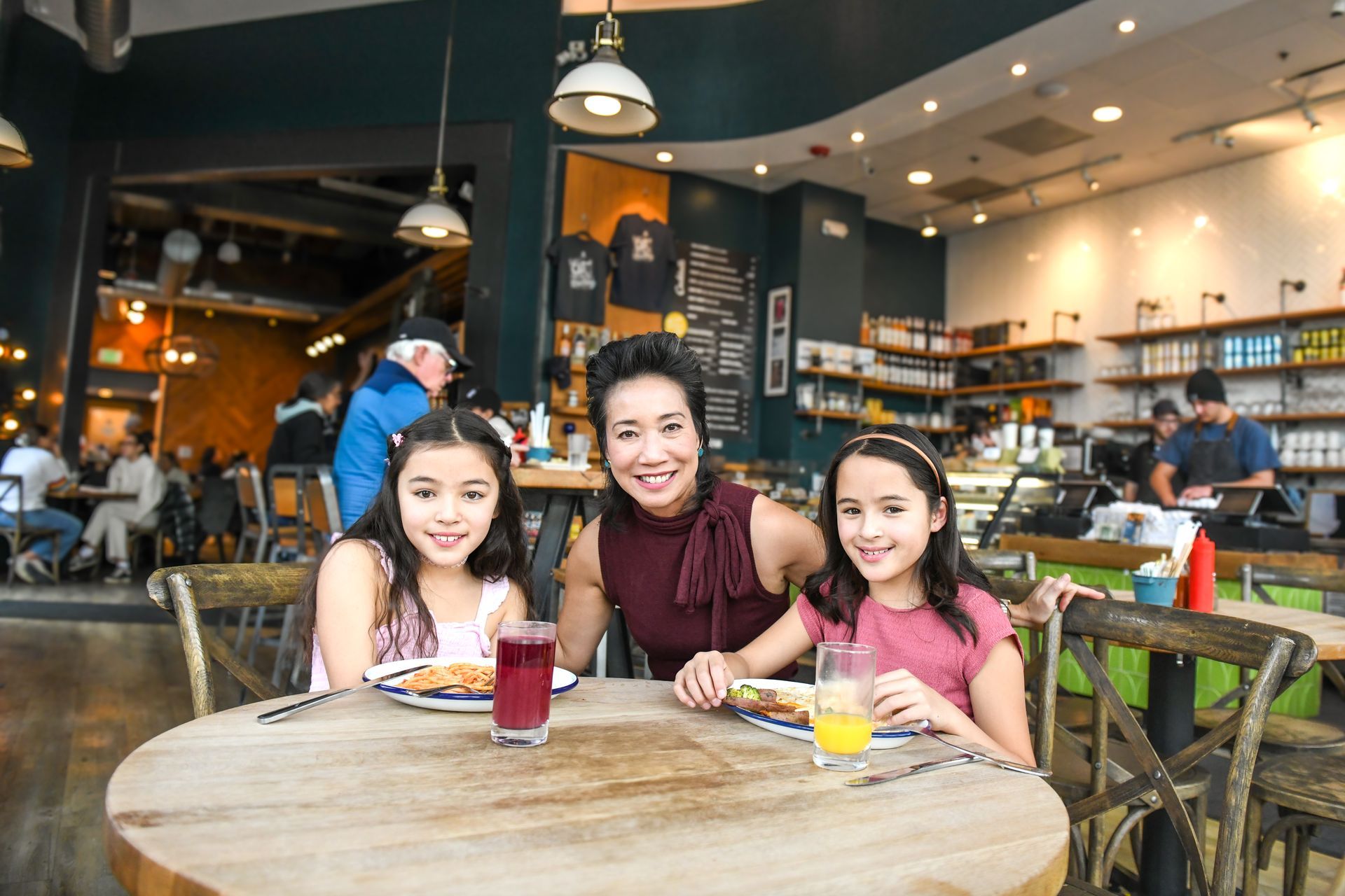 Three people smiling at a café table with drinks in a bright, modern coffee shop