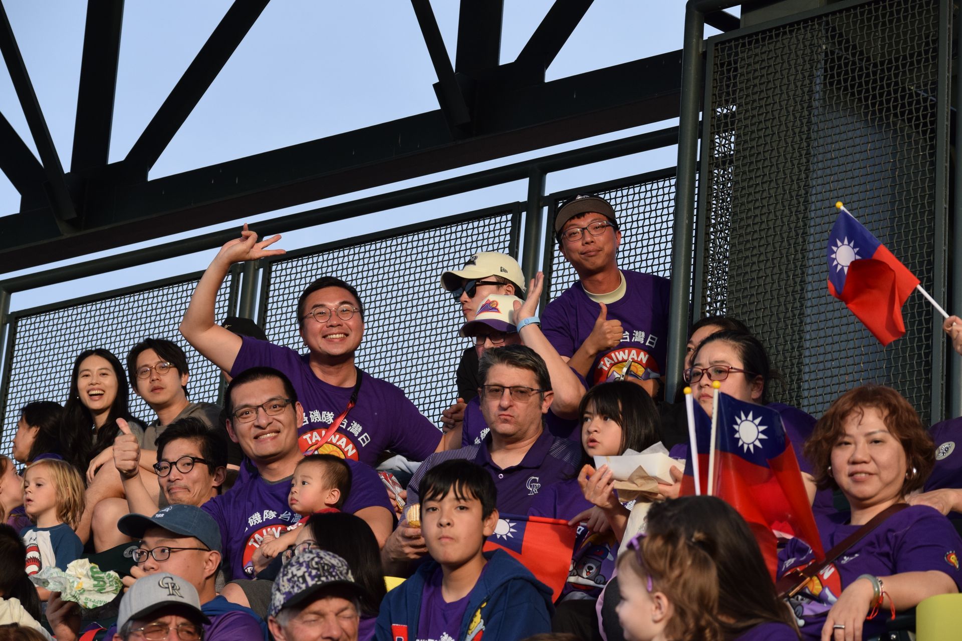People wearing purple cheering at a stadium, some waving flags of Taiwan.