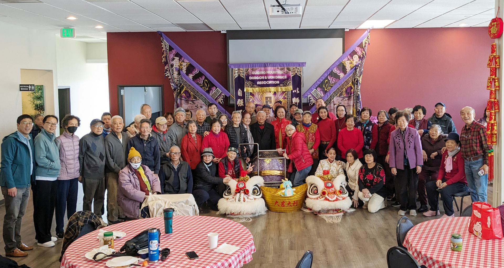 Large group posing in a decorated room with tables, purple streamers, and a festive backdrop