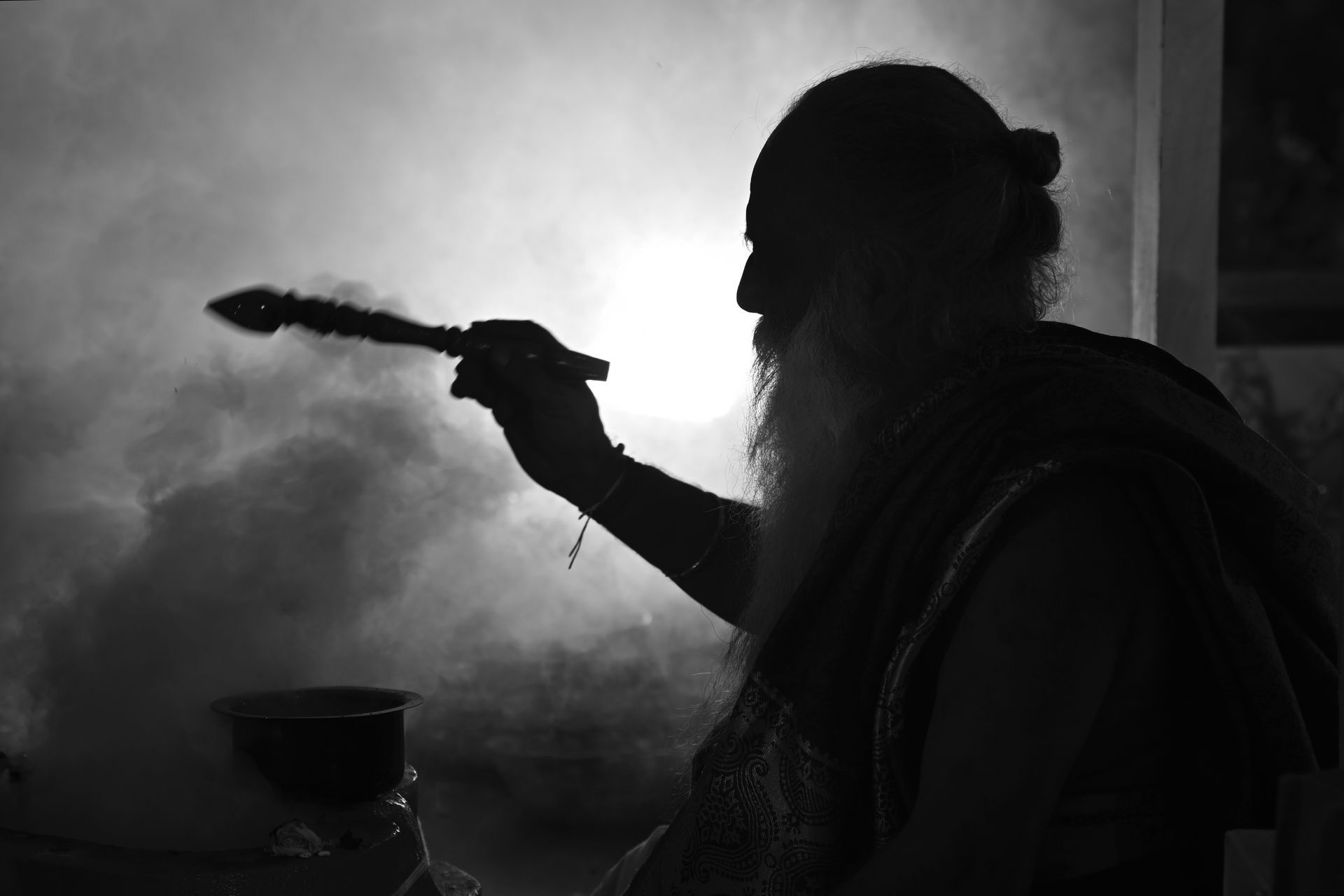 Silhouette of a man with a long beard, holding a smoking bundle, incense ceremony.