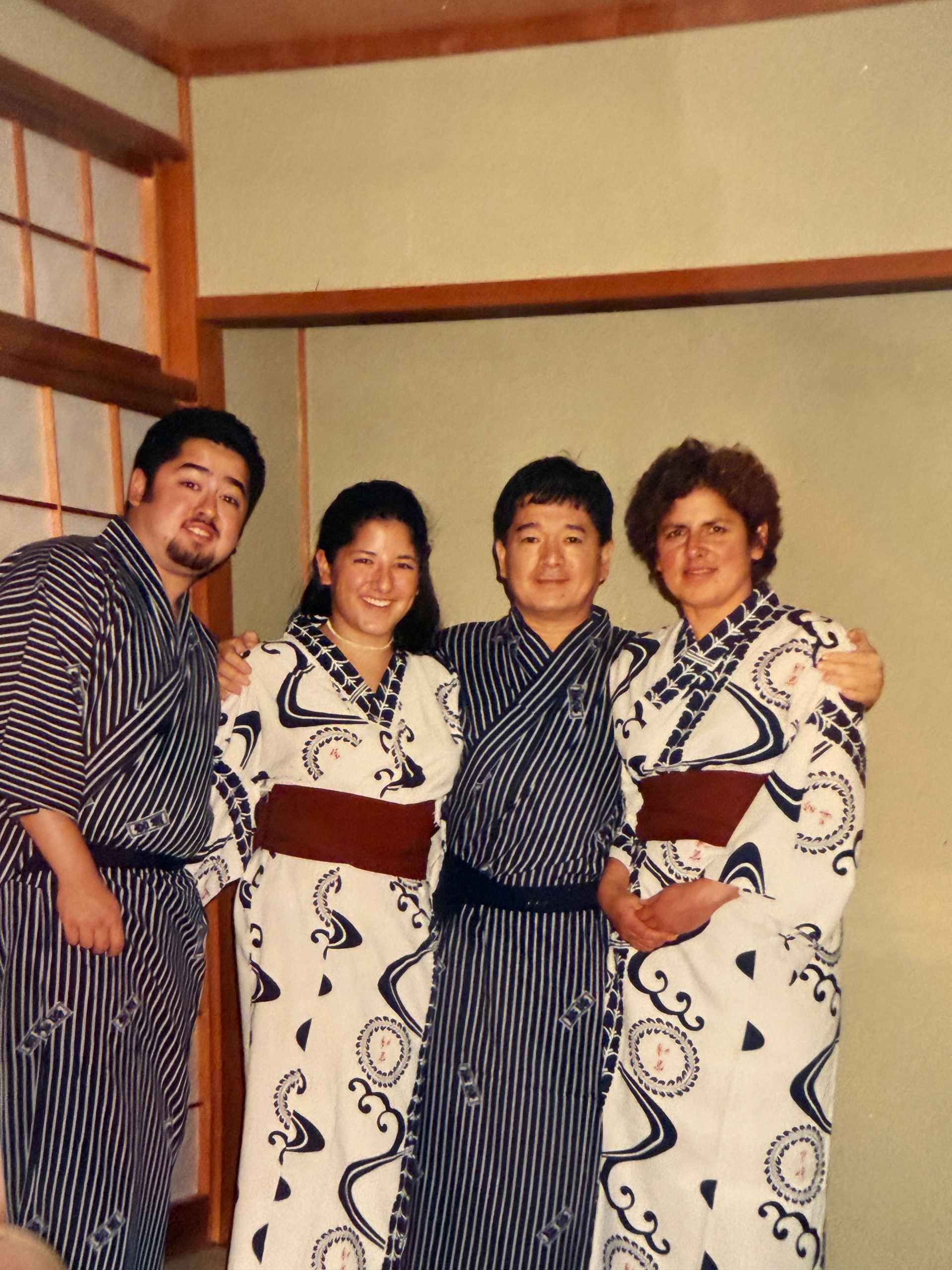 Four people in patterned yukatas posing indoors, smiling and standing close together.