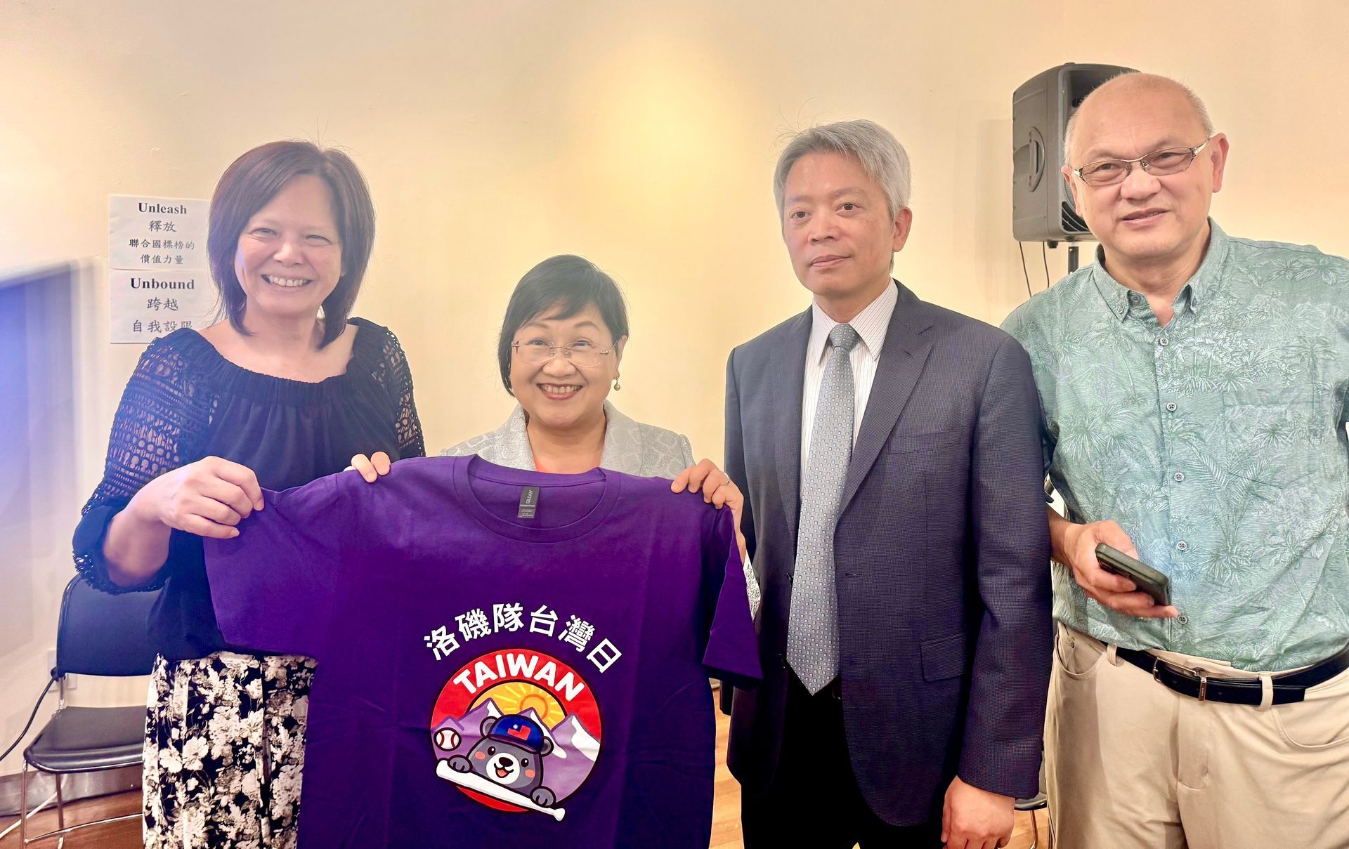 Four people holding up a purple Taiwan t-shirt indoors. The shirt has a bear graphic and text.