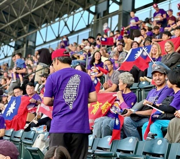 People with Taiwan flags at a baseball game, many wearing purple shirts.