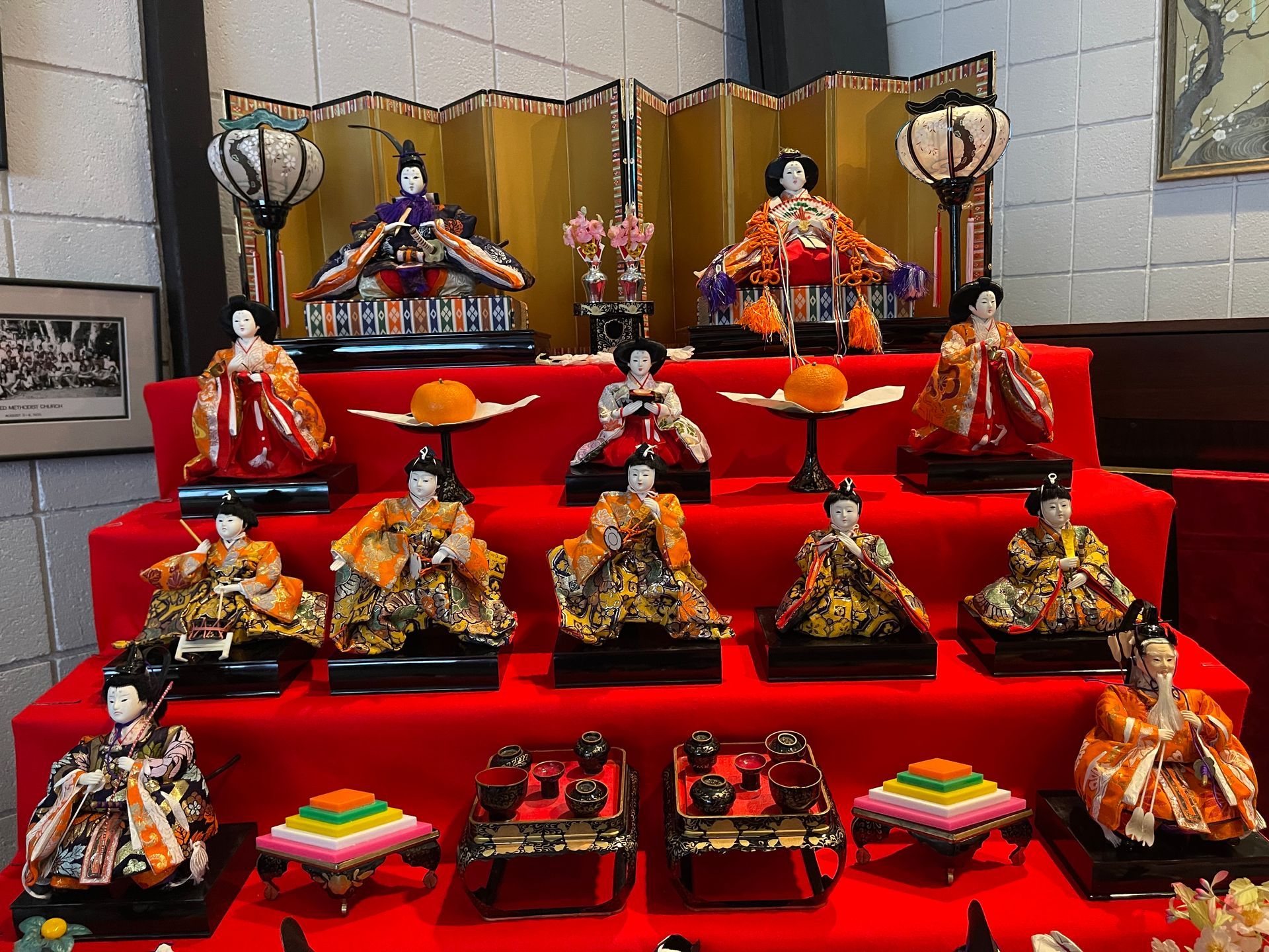 Japanese Hina dolls on red tiered display. The dolls wear traditional colorful garments, gold screen backdrop.