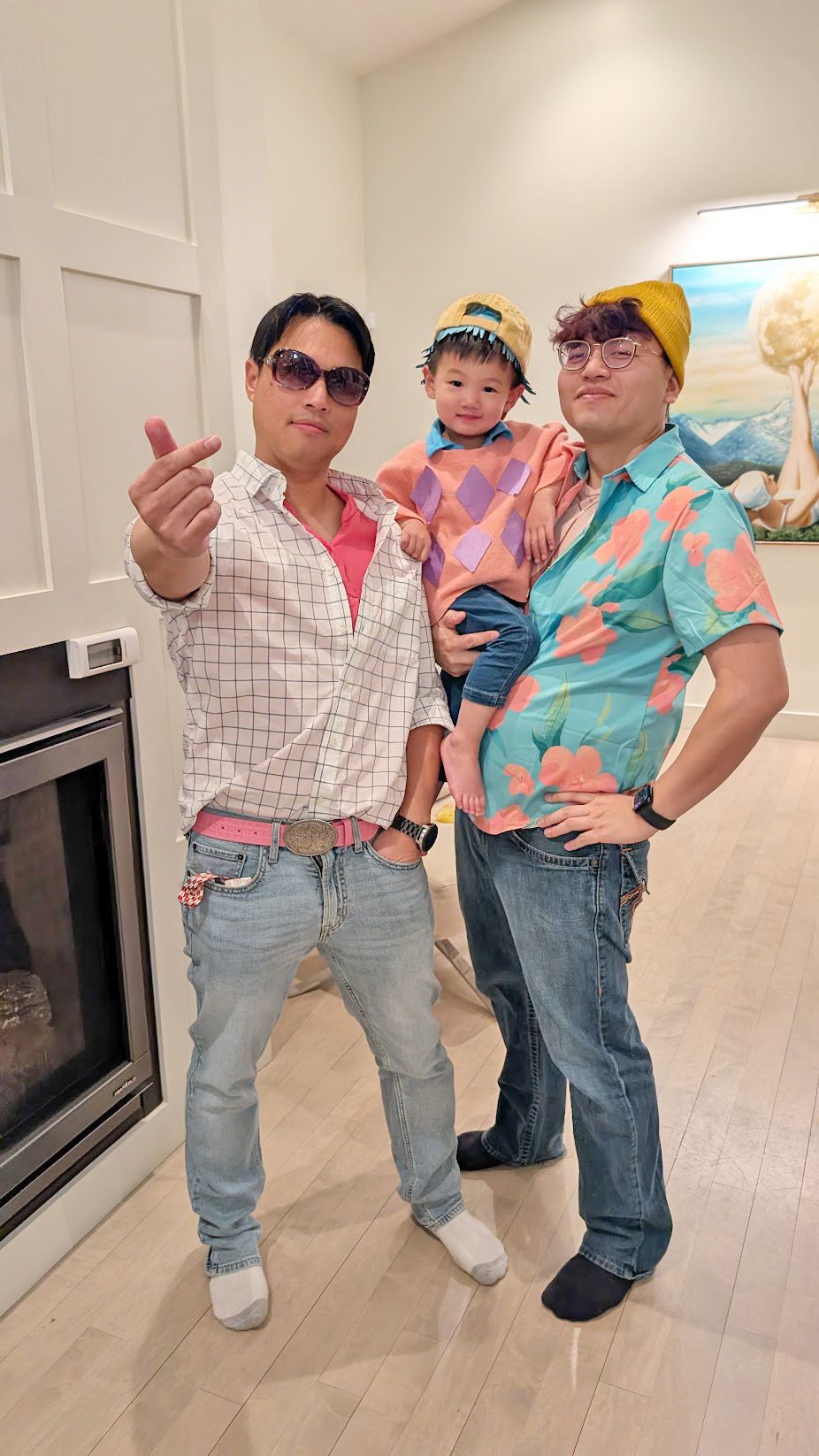 Three people posing: Man with sunglasses, child, man in floral shirt, fireplace.