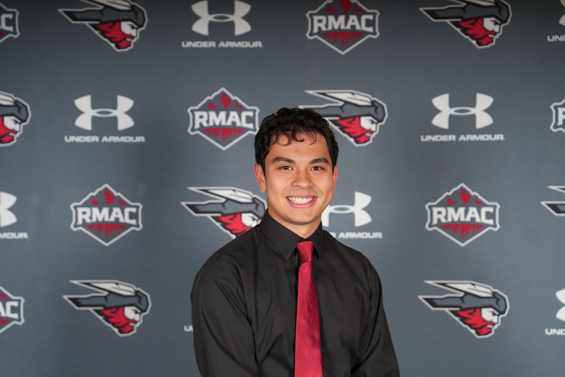 Kai Vong smiles in front of a RMAC/Under Armour backdrop for headshot.