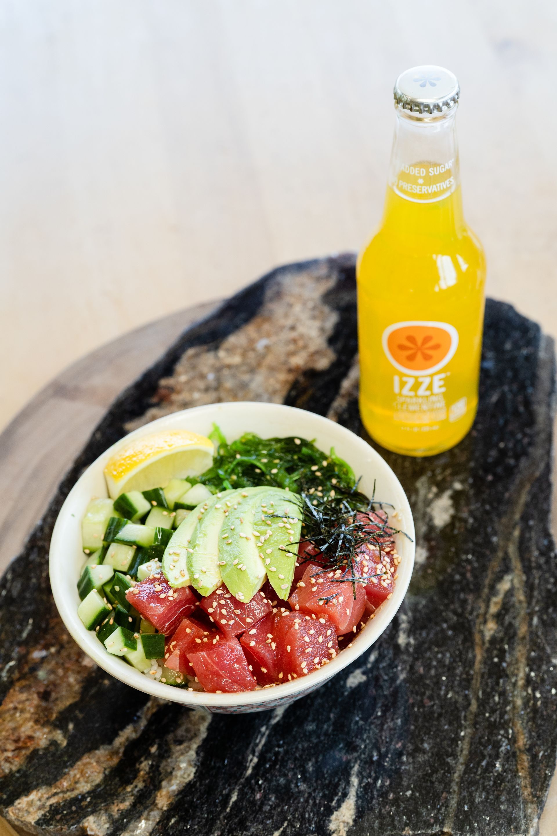 Acai bowl with berries, banana, and mint on a dark stone table beside a yellow juice bottle.