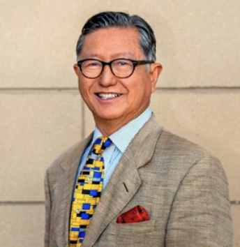 Smiling man wearing glasses, patterned tie, suit jacket, and a pocket square.