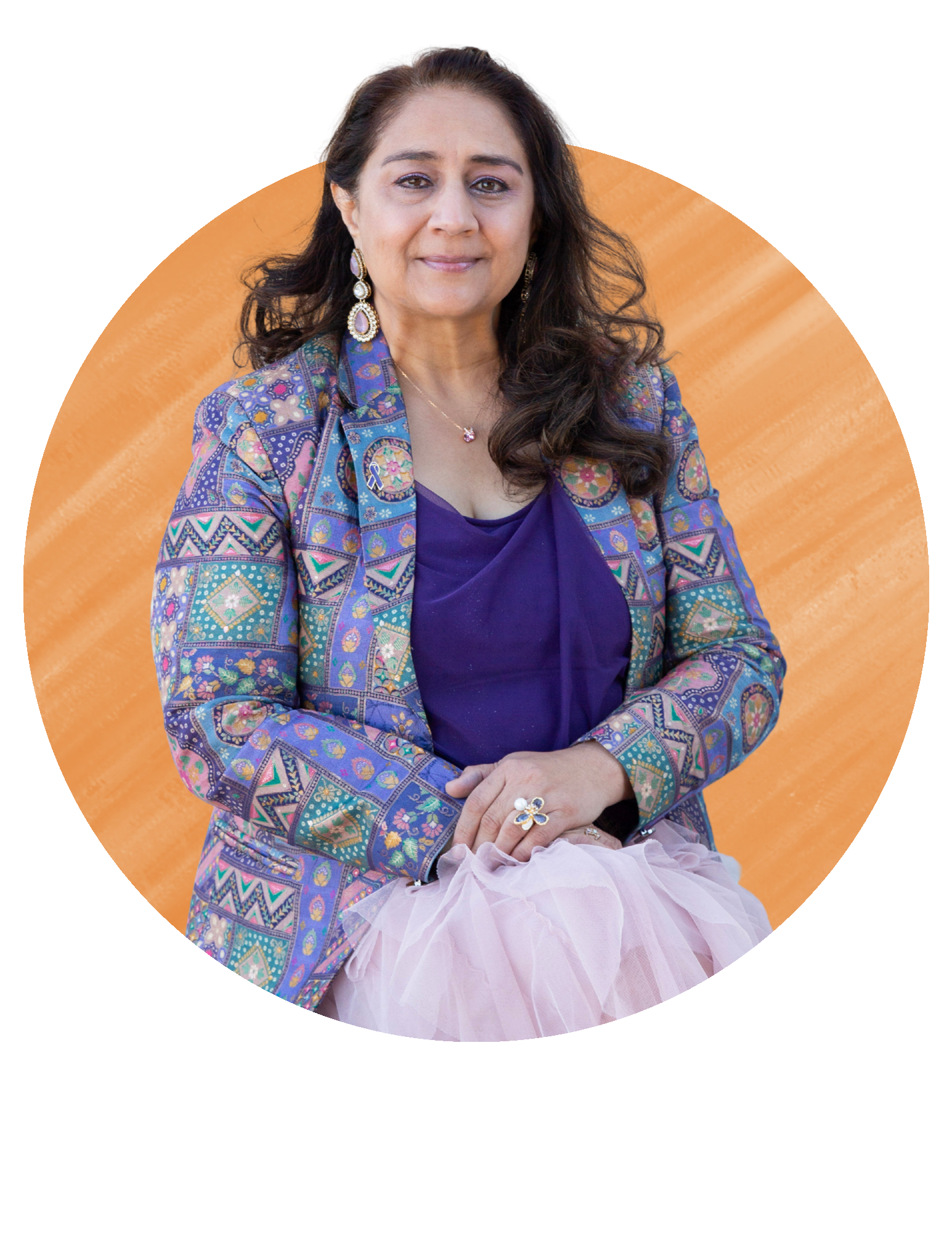 Woman seated against an orange background, wearing a colorful jacket over a purple top and light pink skirt.