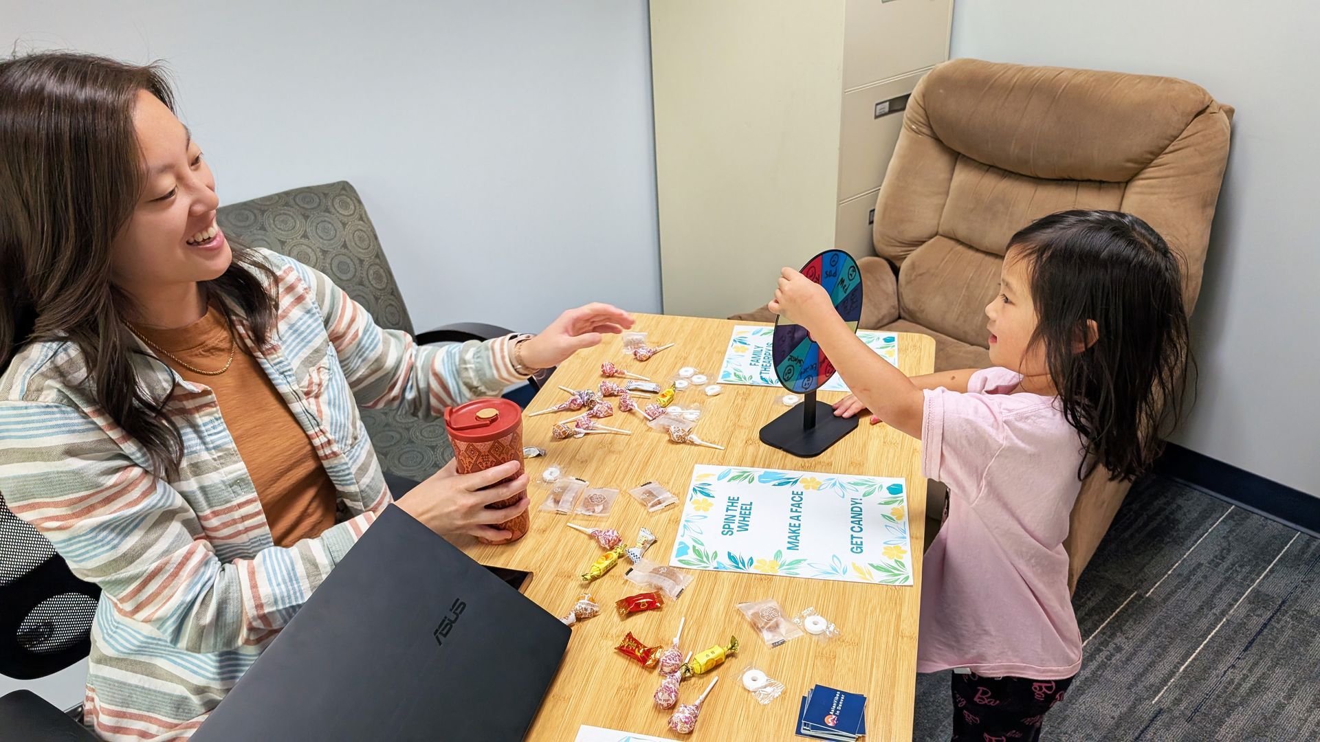 Woman and young girl smiling, playing with colorful toys at a table. Office setting.