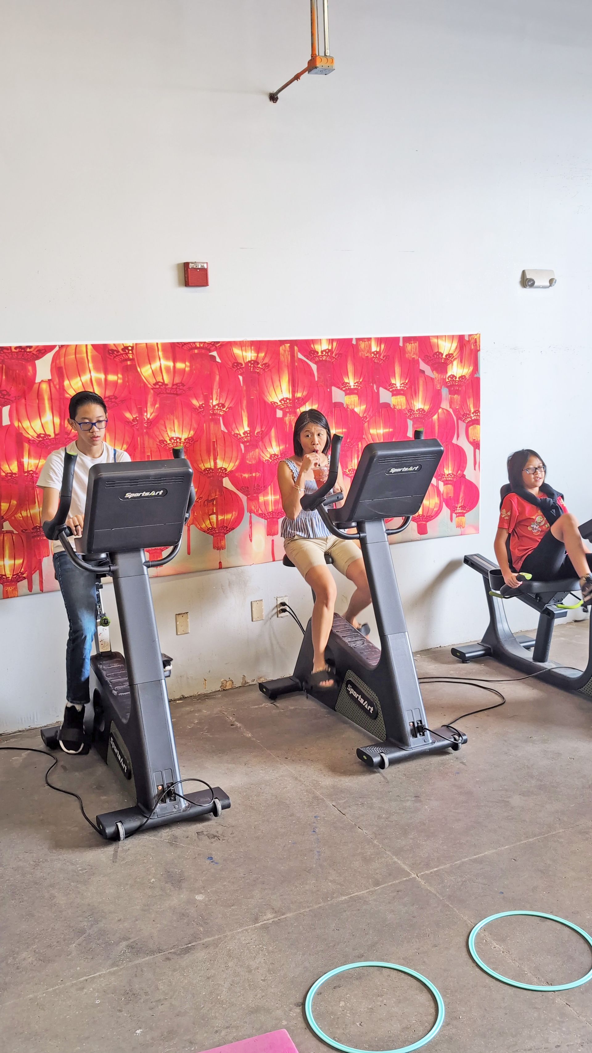Three people on stationary bikes in a gym with a colorful backdrop.