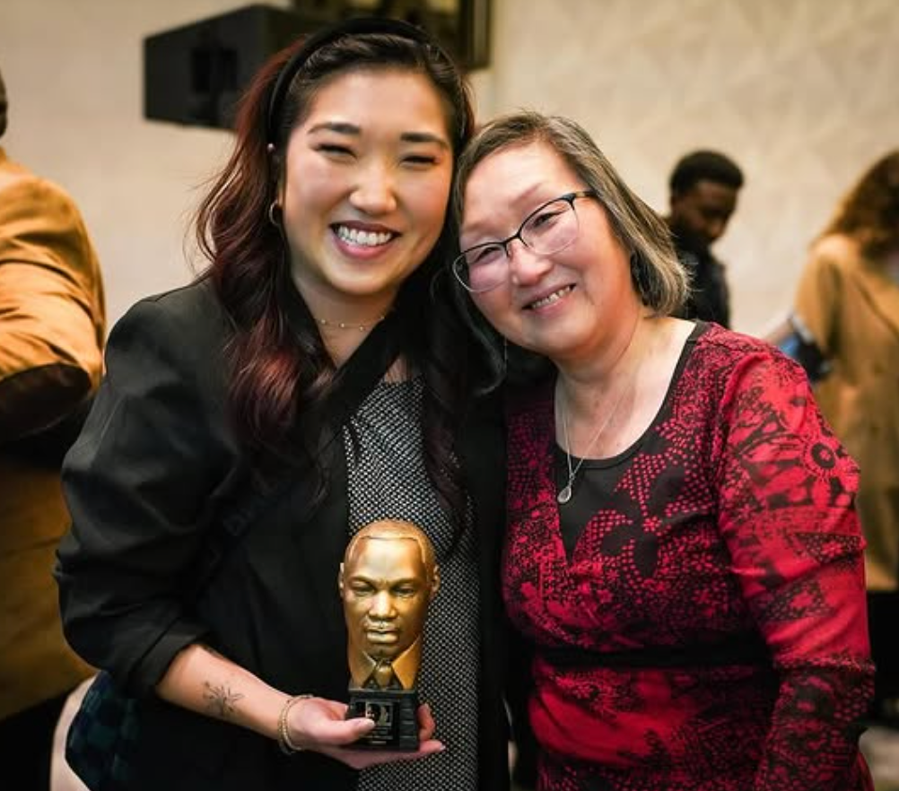 Two women smiling and holding a gold trophy at an indoor event