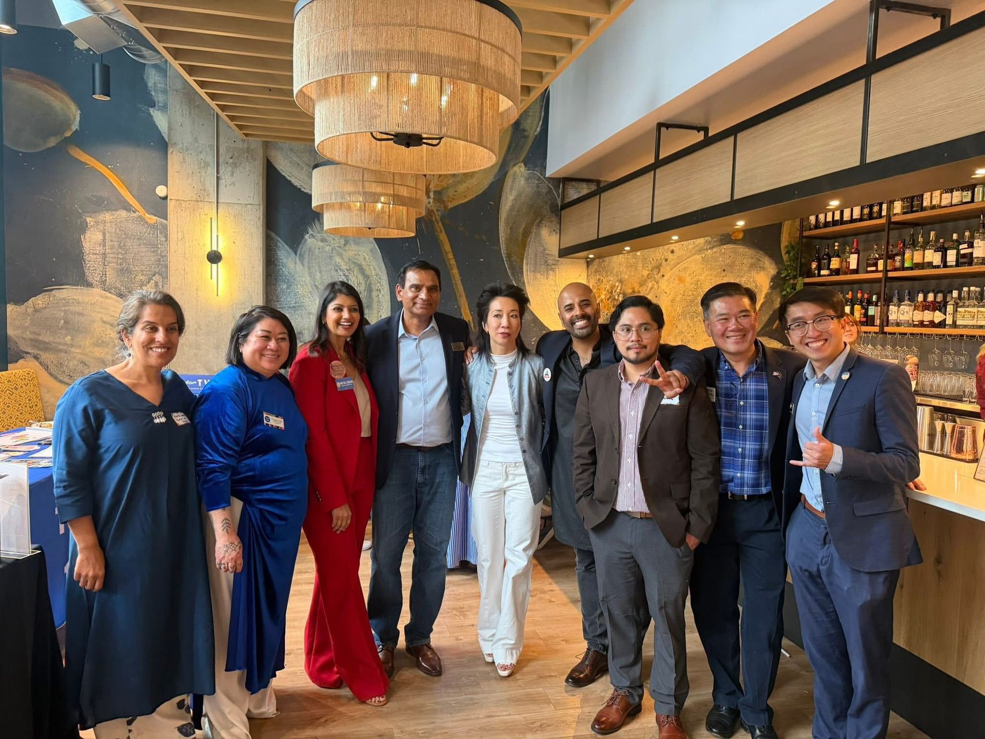 Group of people posing in a stylish restaurant with chandeliers, smiling and dressed in formal and colorful attire