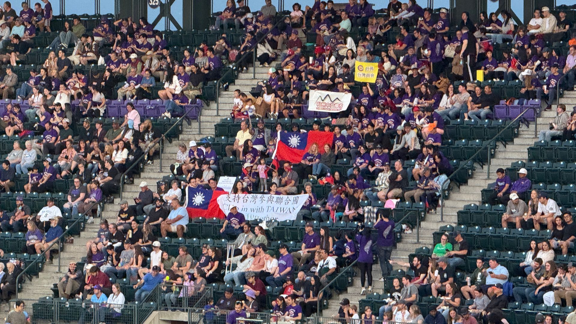 Crowd in a stadium, primarily wearing purple. People hold flags of Taiwan and banners.
