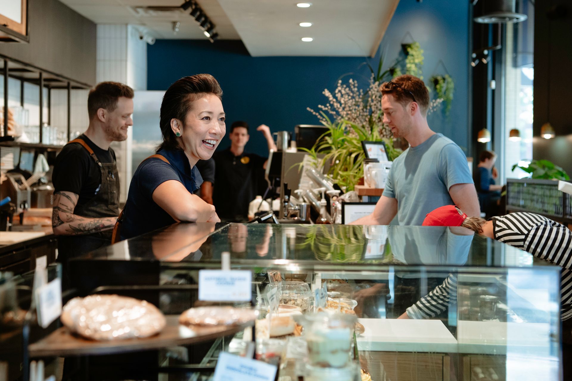 Cafe staff serving customers at a glass pastry counter in a bright modern bakery.