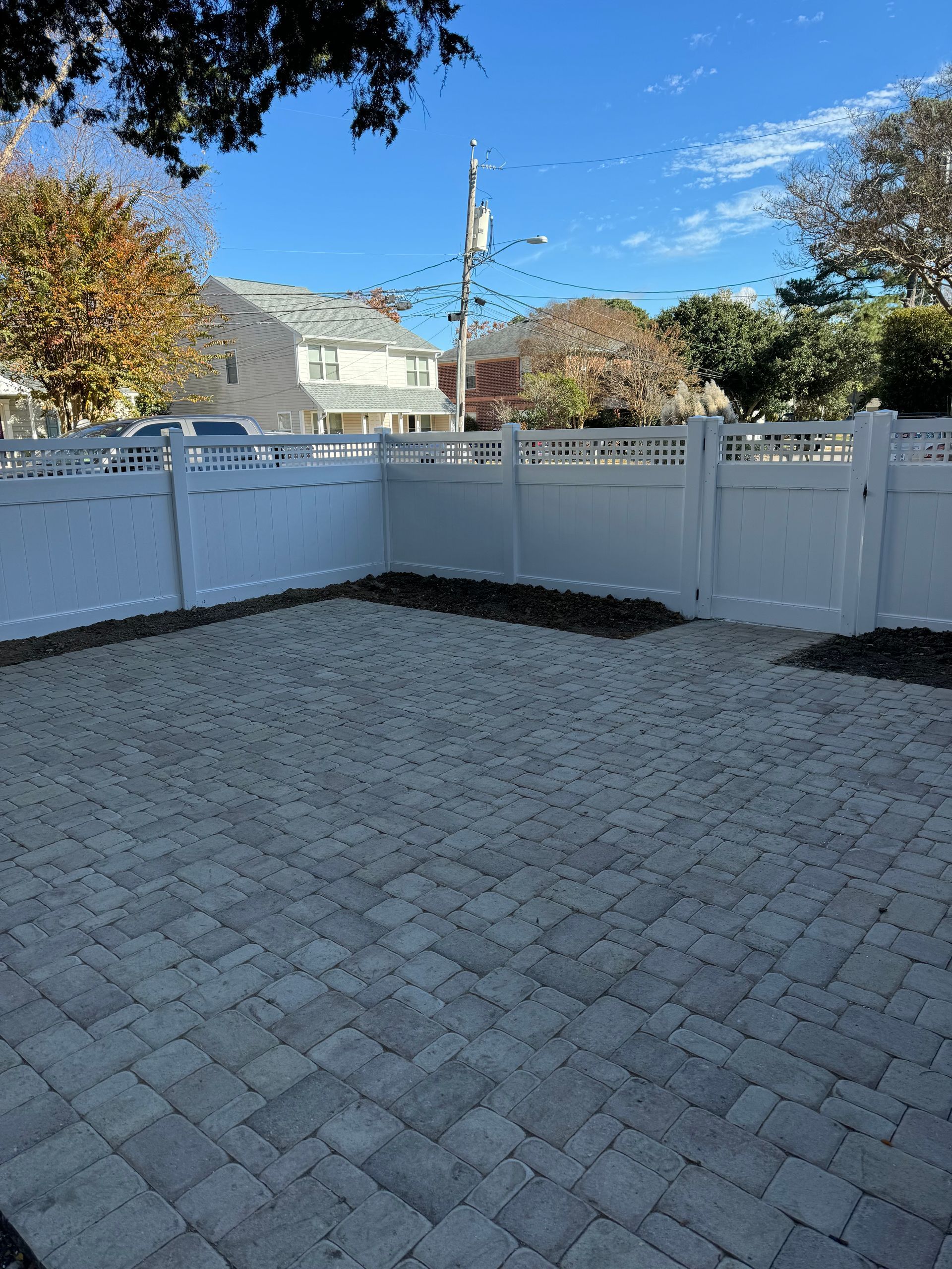 Brick patio enclosed by white fence; houses and blue sky in background.