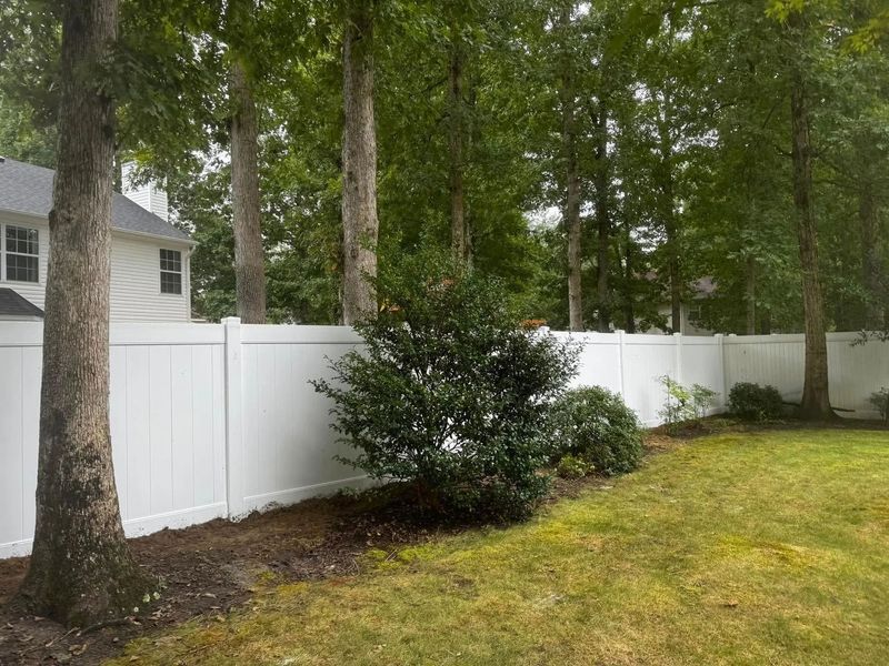 White vinyl fence lines a backyard, trees in the background.