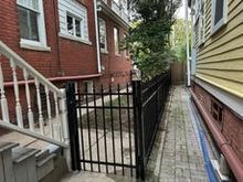 Black metal fence encloses a narrow walkway between brick and yellow buildings.
