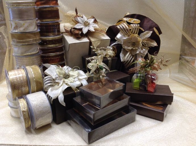 Pile di scatole regalo nelle tonalità del marrone e dell'oro, decorate con fiocchi, nastri e motivi floreali.