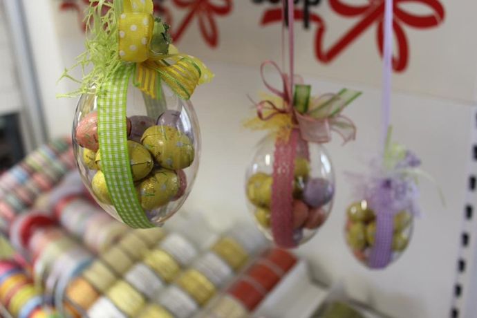 Tre ornamenti in plastica trasparente riempiti con piccole uova di caramelle colorate, ognuno legato con un diverso nastro decorativo.