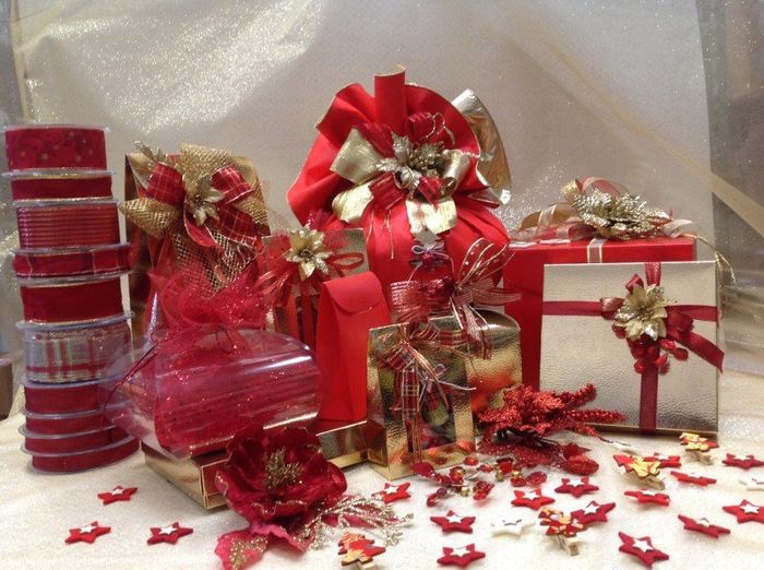 Una collezione di scatole regalo incartate nei toni del rosso e dell'oro, decorate con fiocchi e coriandoli a forma di stella.