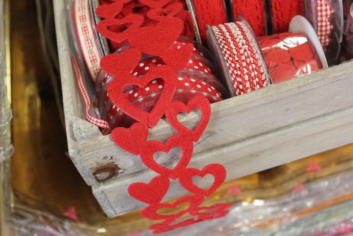 Un nastro di feltro rosso con ritagli a forma di cuore drappeggiato su una rustica cassa di legno piena di vari rotoli di nastro.