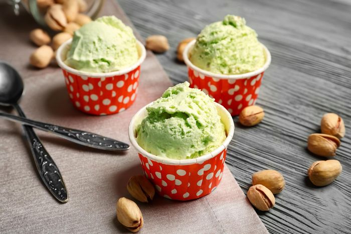 Tre coppette di gelato al pistacchio in bicchieri di carta a pois rossi, con pistacchi sparsi su una superficie di legno.