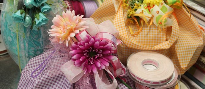 Tre articoli confezionati per un regalo, decorati con motivi floreali e nastri, tra cui carta e tessuto a quadretti.