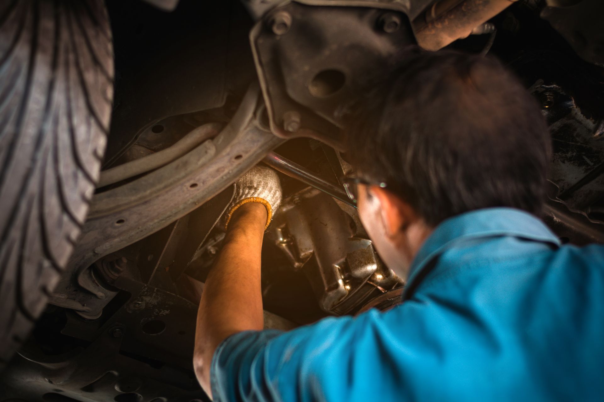 Mechanic standing underneath a car working on the transmission.