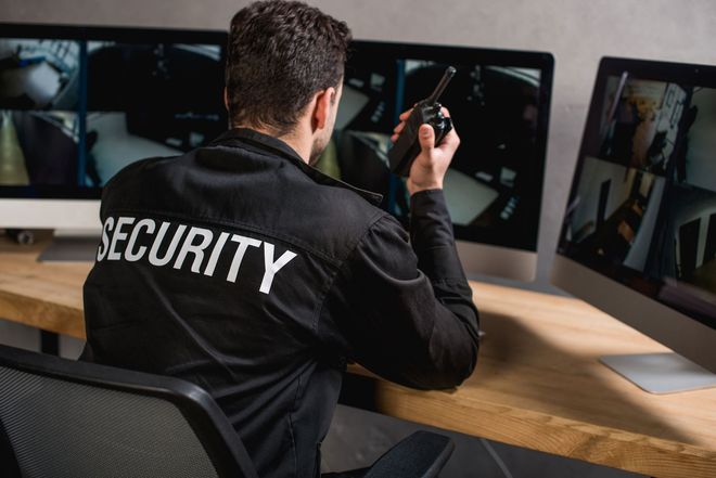 A security guard is sitting at a desk talking on a walkie-talkie.