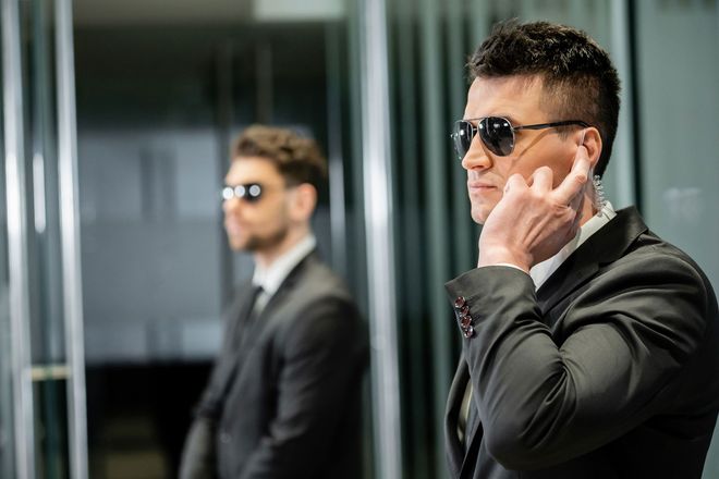 Two security guards wearing suits and sunglasses are standing next to each other.