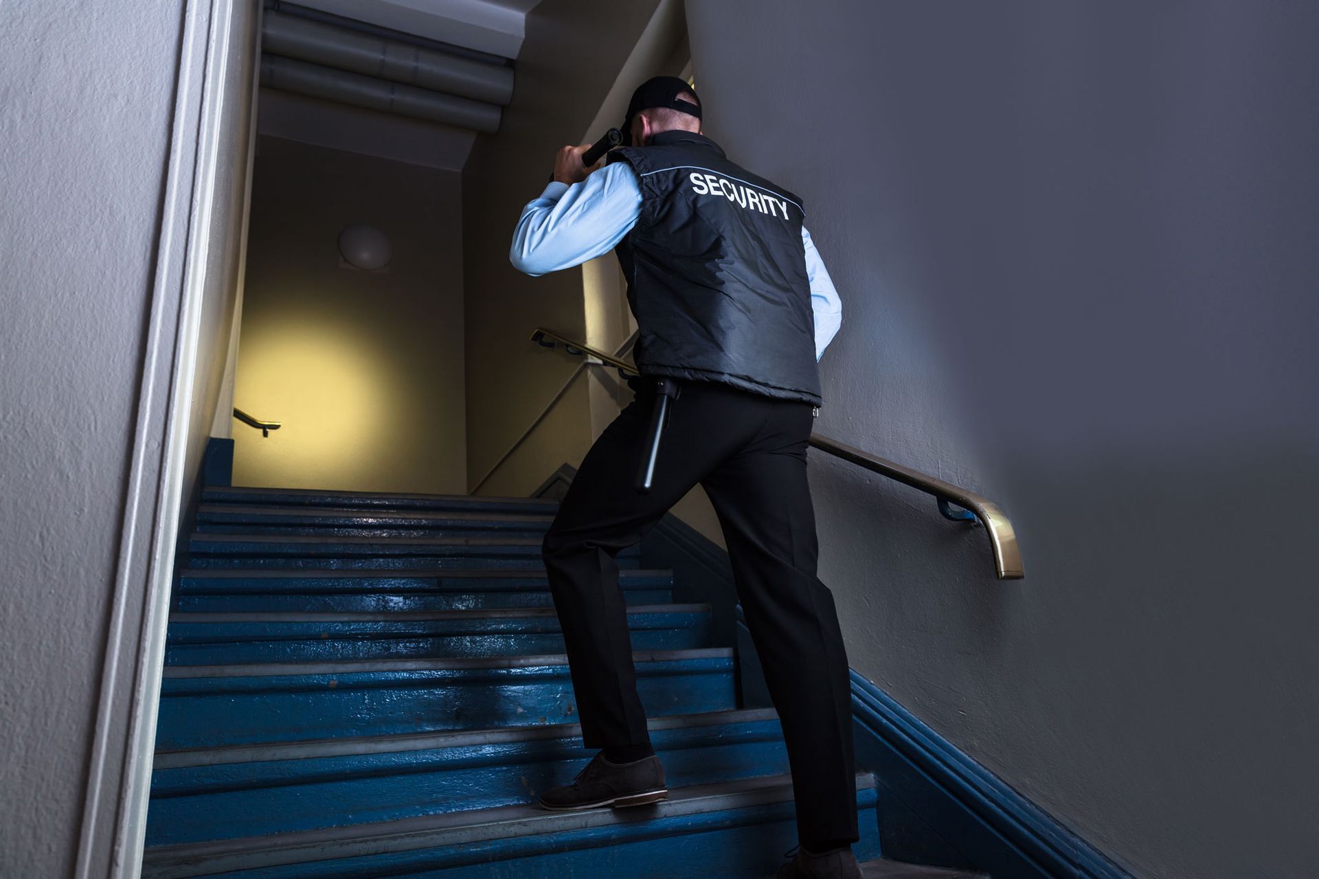 A security guard is walking up the stairs with a flashlight.
