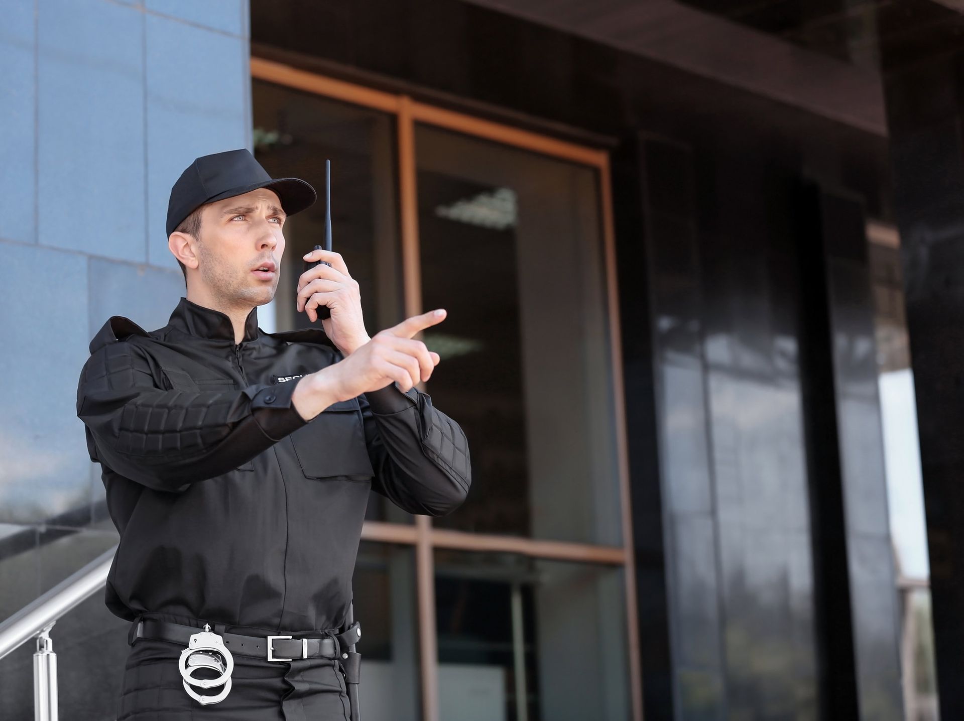 A man in a black uniform is talking on a walkie-talkie in front of a building.