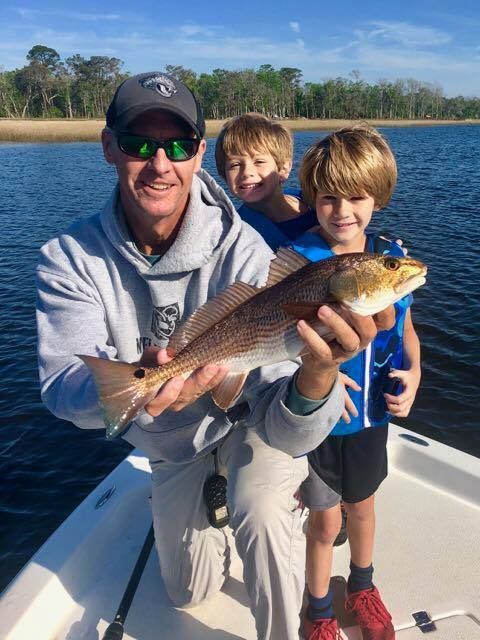 Man and two boys on boat, holding a fish, sunny day.