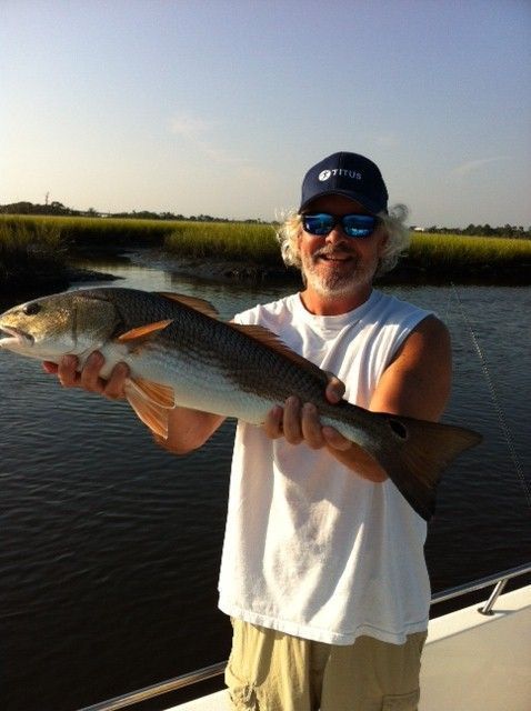 Man holding a redfish on a boat, marsh background.